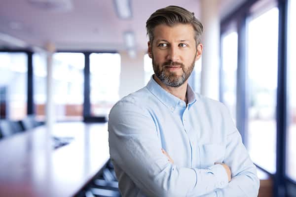 Portrait of confident business man standing with arms crossed in the conference room. Mid aged man wearing shirt and looking away.