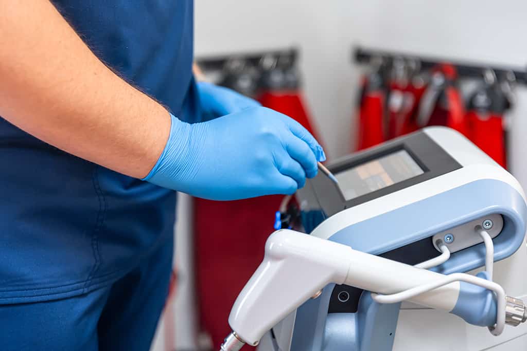 Shock wave therapy device with male doctor hands in rubber gloves.