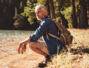 Portrait of a mature man sitting next to a lake admiring the view. Male hiker relaxing by a lake and looking away at a view.